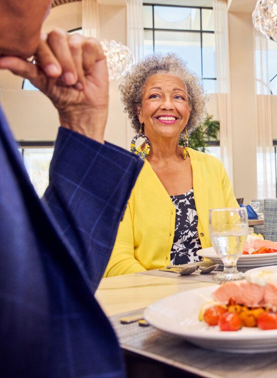 group of senior friends smile and enjoy an elegant dinner together at Village on the Green Senior Living Community