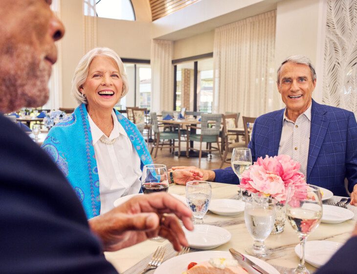 group of senior friends smile and enjoy an elegant dinner together at Village on the Green Senior Living Community
