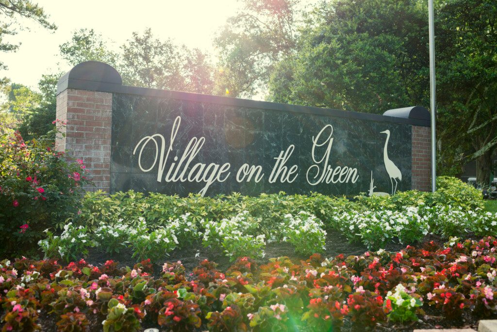 Village on the Green entrance sign, surrounded by tropical foliage