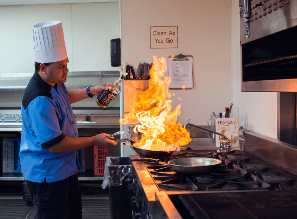 chef prepares complex dish in pan, which flames briefly from wine being poured in