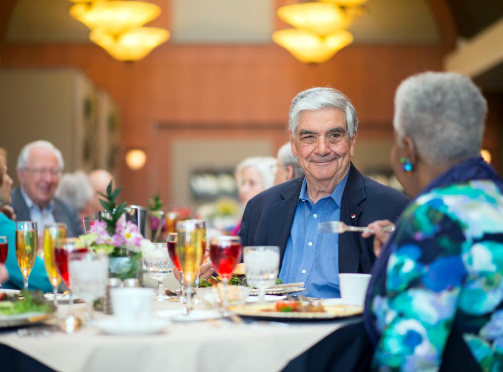 group of well-dressed senior friends enjoy an elegant dinner and drinks together at their senior living community