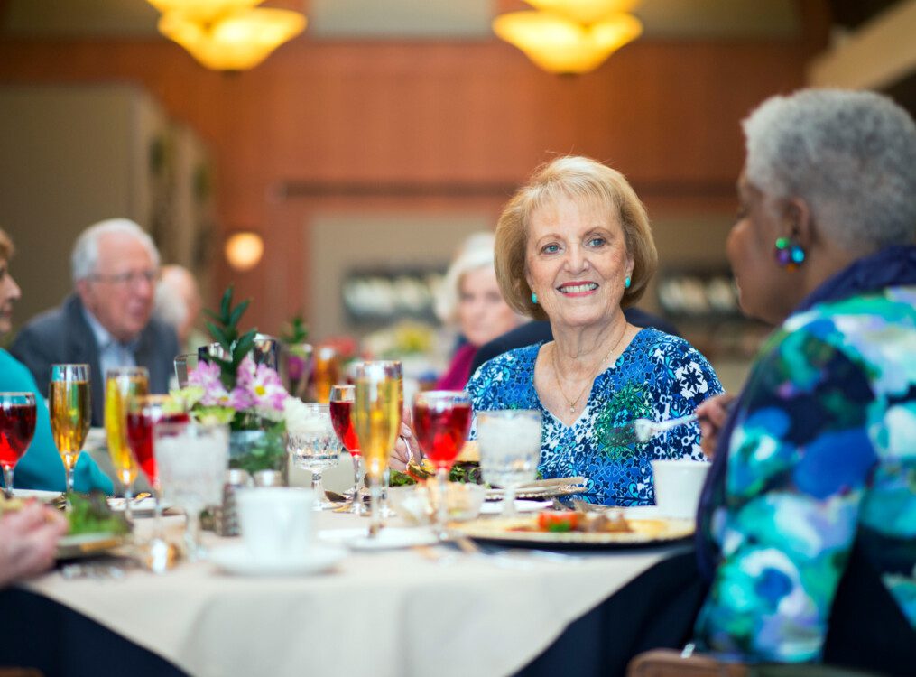 senior woman smiles at her companions during an elegant dinner at her senior living community