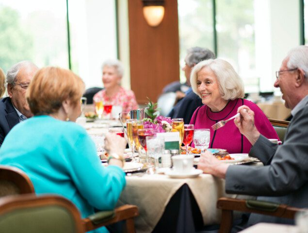 group of elegantly dressed senior men and women smile while enjoying a high-end dinner at their senior living community