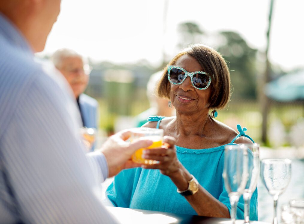 stylish senior woman in blue sunglasses accepts cocktail from bartender outdoors at her senior living community
