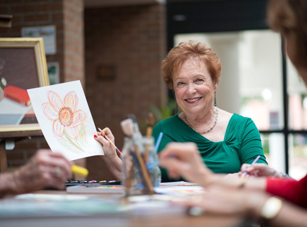 senior woman smiles and shows off her artwork to her friends during a class