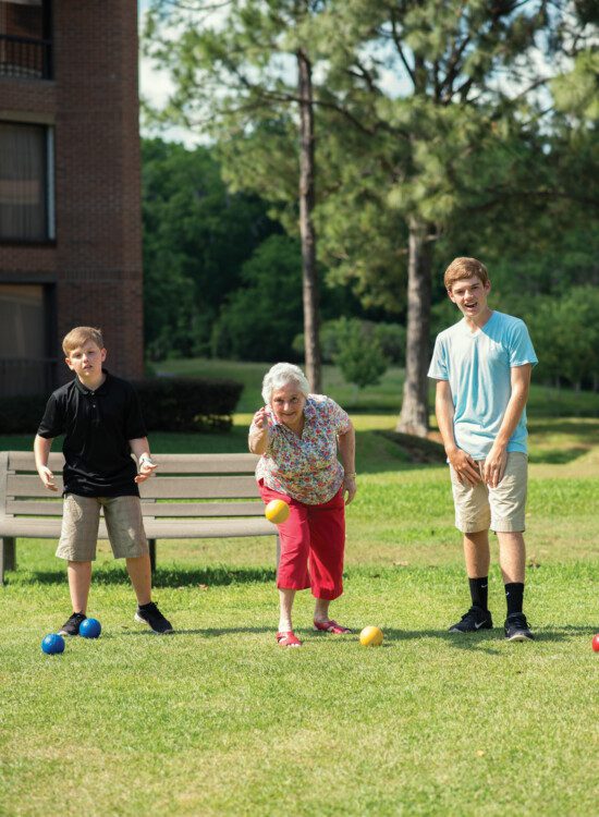 senior woman plays bocce ball with her grandsons outside of her senior living community