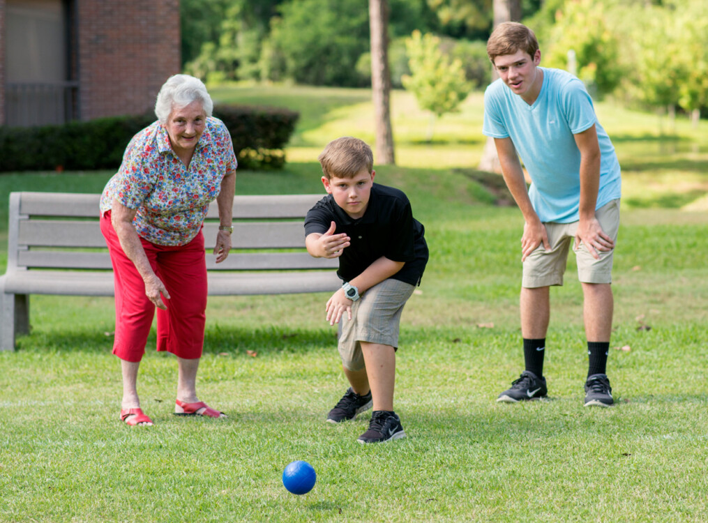 senior woman plays bocce ball with her grandsons outside of her senior living community