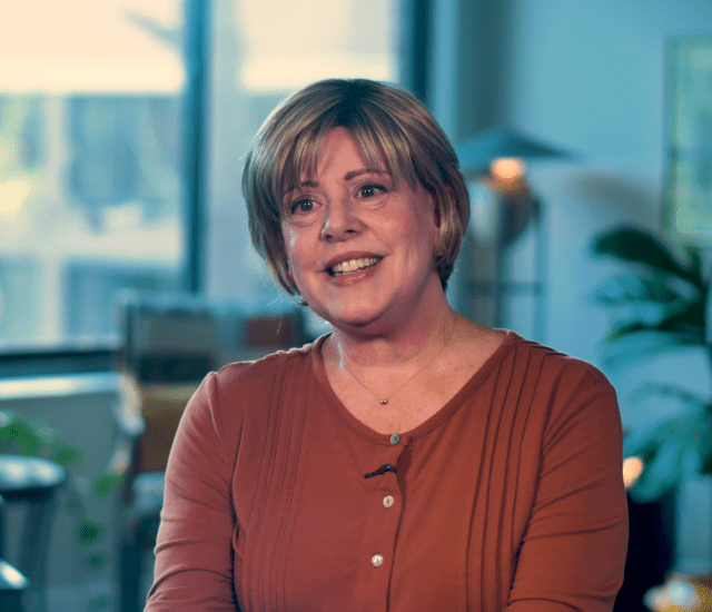 Woman (Susan Craig) in red shirt sits and speaks during an interview