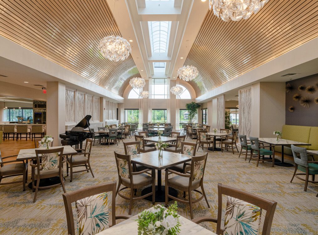 expansive indoor dining area with grand piano and chandeliers at Village on the Green Senior Living Community