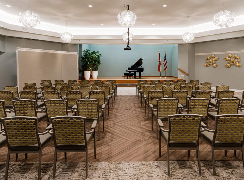 entertainment room with rows of chairs and small stage set with a grand piano