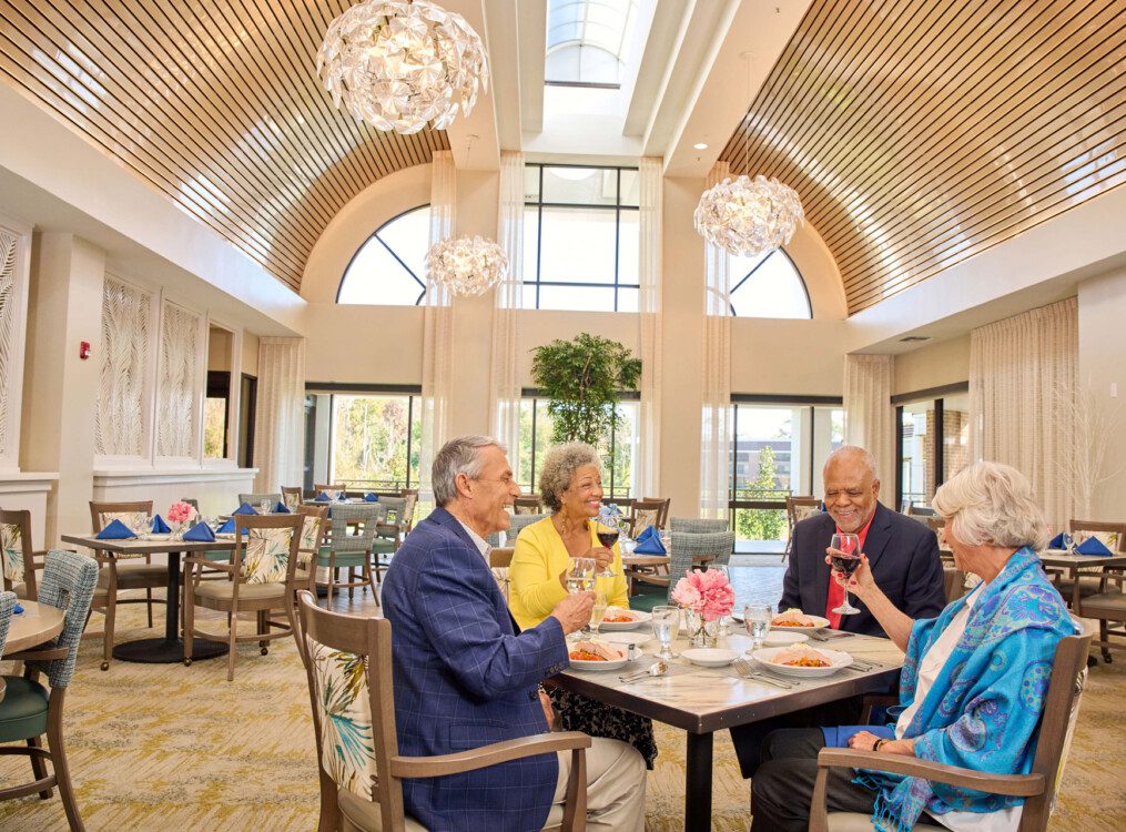 group of senior friends smile and enjoy an elegant dinner together at Village on the Green Senior Living Community