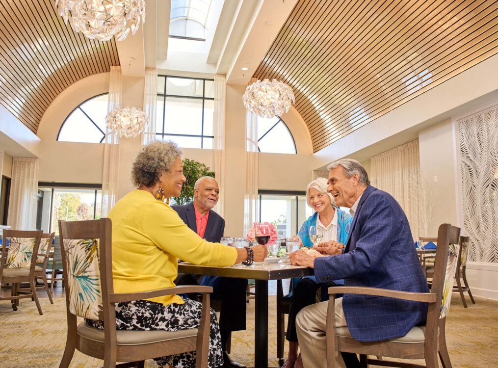 group of senior friends smile and enjoy an elegant dinner together at Village on the Green Senior Living Community