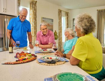 group of senior friends enjoy wine and dinner together in one of the villas at Village on the Green Senior Living Community