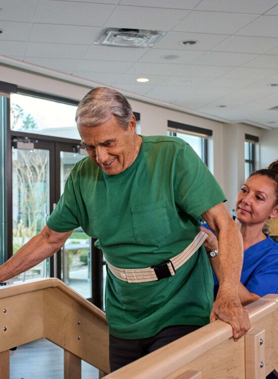 senior man performs physical therapy exercise with the help of a PT in at Village on the Green Senior Living Community