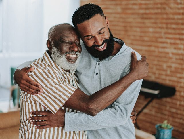 Senior father and adult son happily hugging.