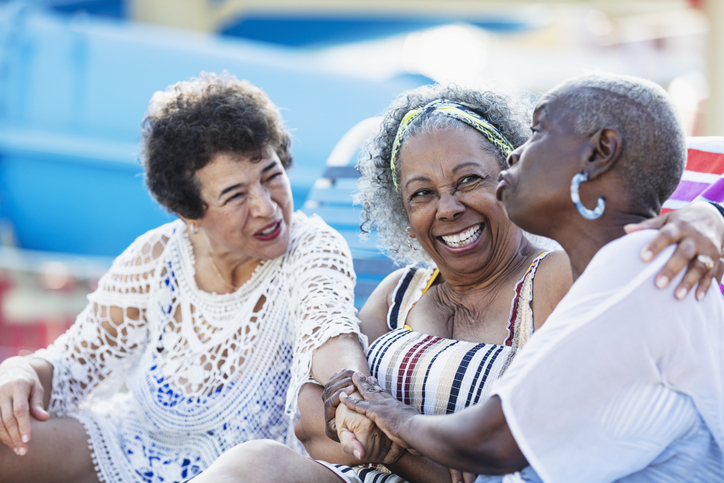 Three multiracial senior women on lounge chairs talking