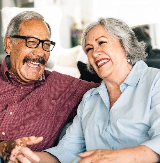 Older couple laughing together on a couch, looking happy and relaxed.